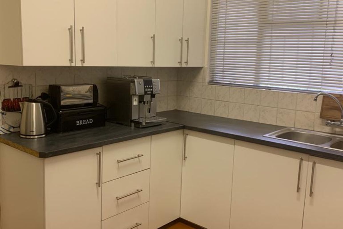 A functional kitchen featuring white cabinetry, dark laminate countertops, a stainless steel sink, and tiled flooring.