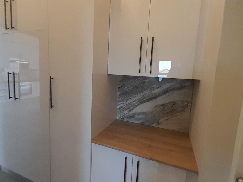 A clean, modern scullery or prep area featuring white high-gloss cabinetry, a wooden countertop, and a decorative marble-look splashback.