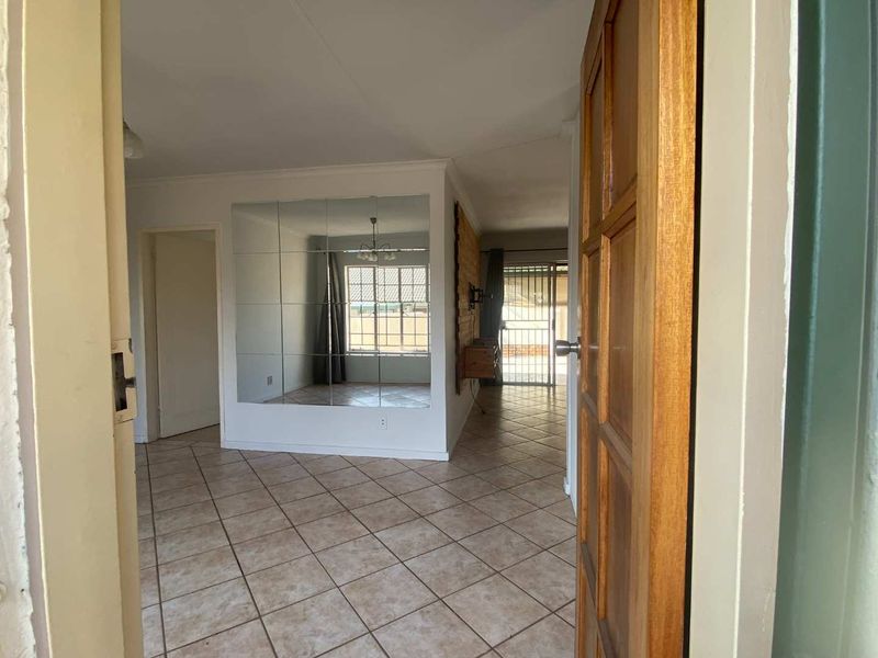 An open-plan living area featuring tiled flooring and a large mirrored wall feature, viewed from the entrance doorway.