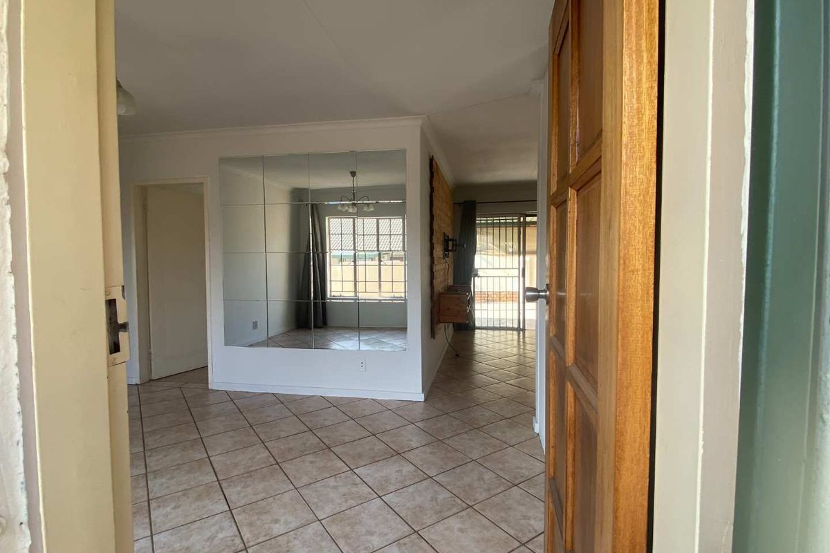 An open-plan living area featuring tiled flooring and a large mirrored wall feature, viewed from the entrance doorway.