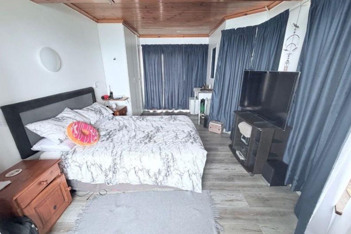 A bedroom featuring a timber-paneled ceiling, wood-look flooring, and built-in storage cupboards, providing a functional and cozy living space.