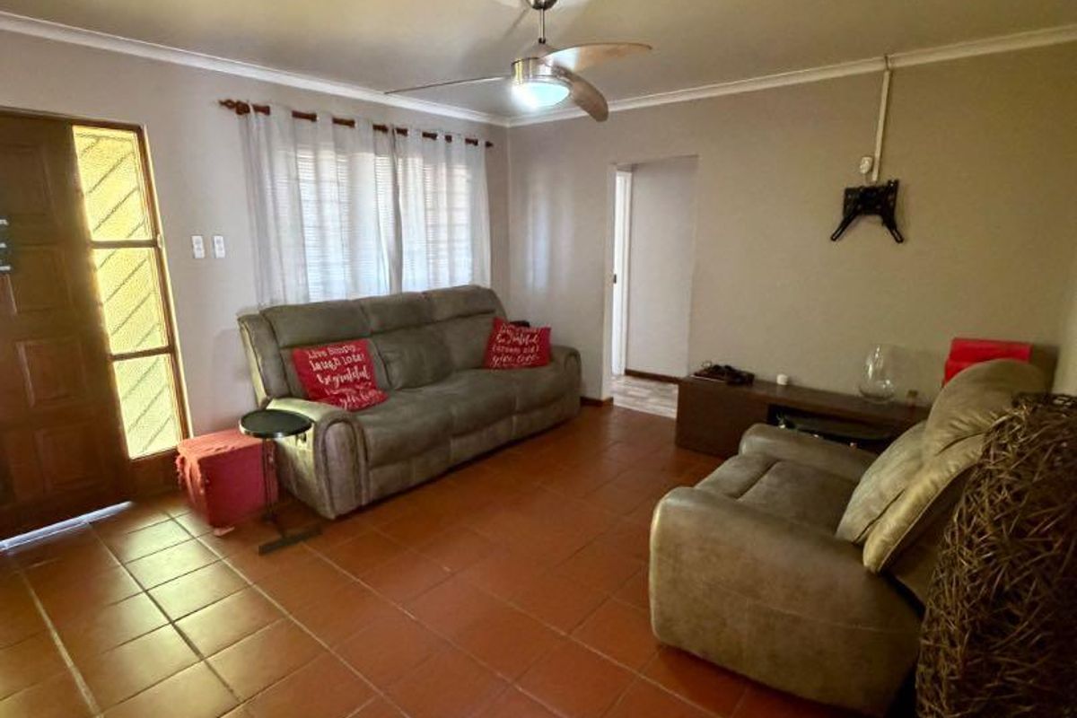 A living room featuring terracotta floor tiles, a ceiling fan, and a timber front door with glass inserts.