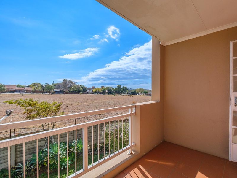 A covered balcony featuring tiled flooring, a metal balustrade, and a glass panel door, offering an open view of the surrounding landscape.