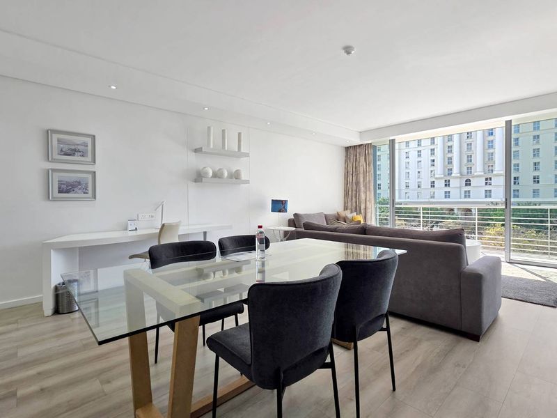 Bright open-plan living and dining area featuring modern laminate flooring, recessed lighting, a built-in desk, and large sliding doors leading to a balcony.