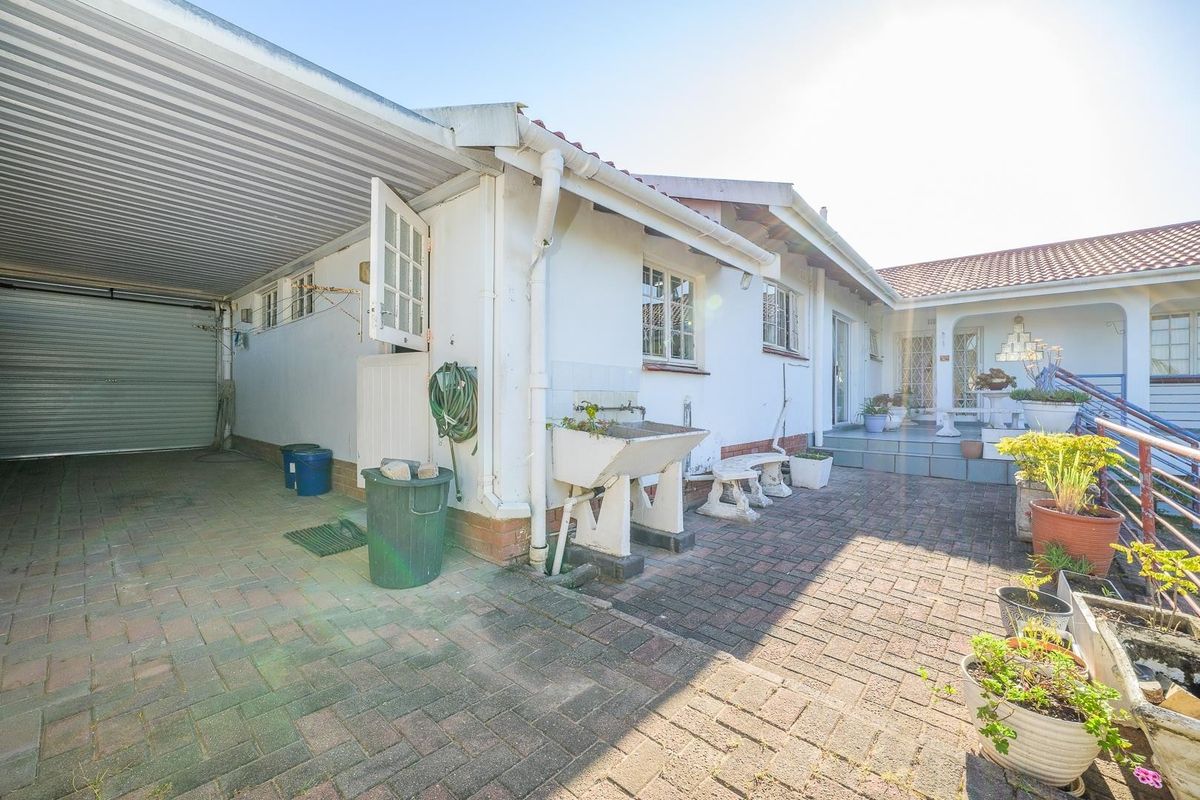 Rear exterior view featuring a paved courtyard, carport, and external utility sink area with access to the main dwelling.