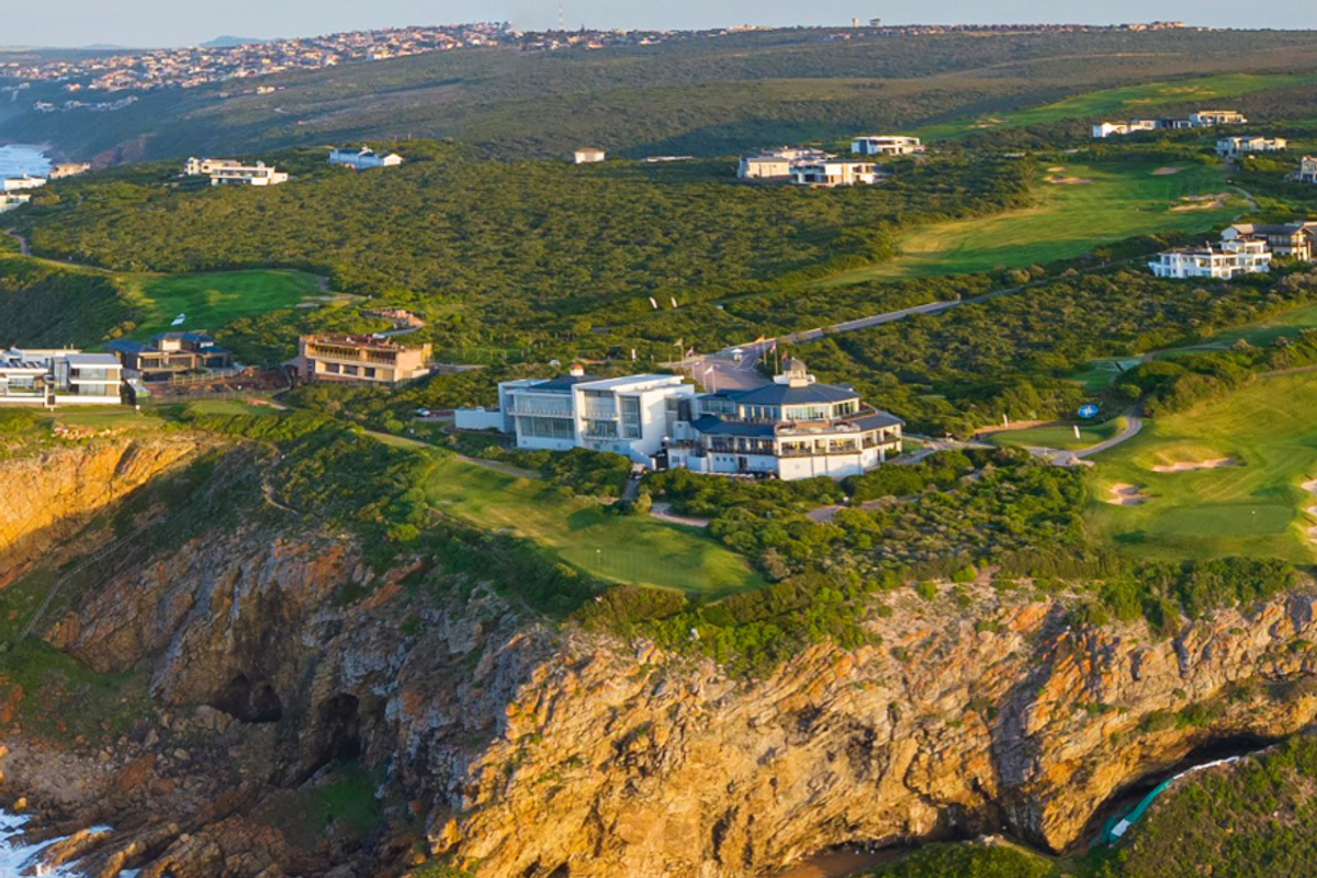 Aerial view of a luxury coastal estate situated on a cliffside, featuring extensive landscaped grounds and proximity to a golf course.