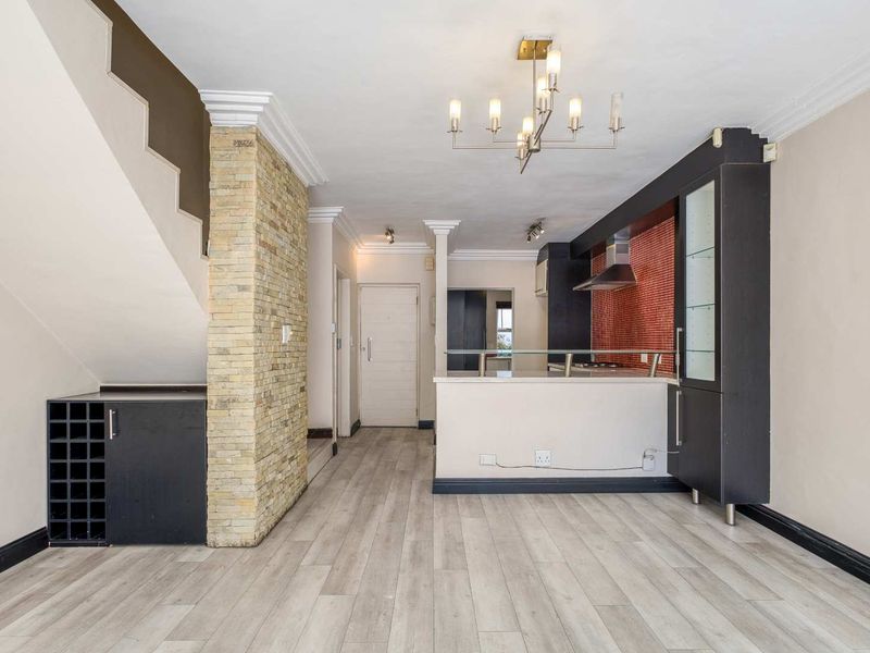 Open plan living area featuring a stone-clad feature wall, built-in wine storage, and a modern kitchen with a breakfast counter and red mosaic backsplash.