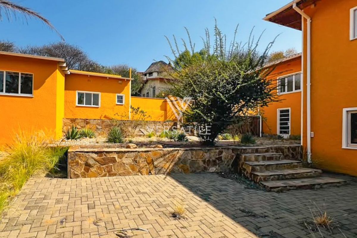 Rear exterior view featuring a paved patio area, stone retaining wall, and steps leading to the garden space.