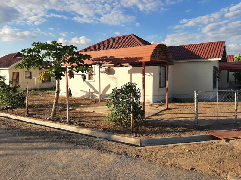 Front view of a single-story house featuring a tiled roof, a metal carport, and a fenced yard with unlandscaped grounds.