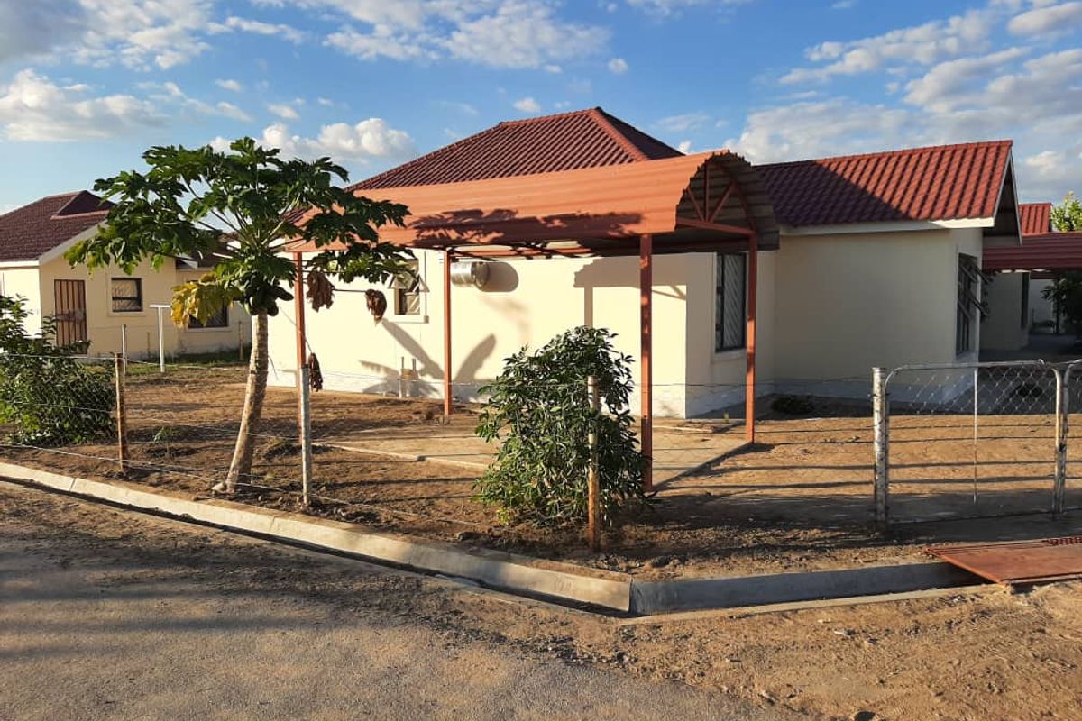 Front view of a single-story house featuring a tiled roof, a metal carport, and a fenced yard with unlandscaped grounds.