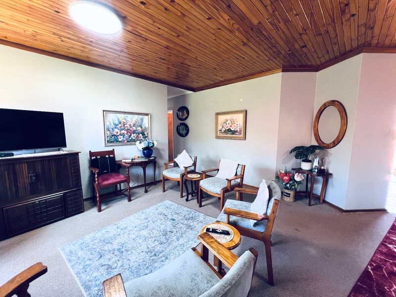 A living room featuring a distinctive timber tongue and groove ceiling and neutral carpeted flooring, offering a traditional and cozy atmosphere.