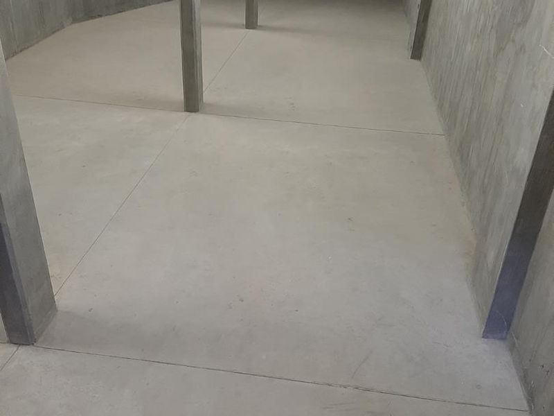 An expansive, unfinished industrial utility space featuring raw concrete flooring, walls, and structural support columns, suitable for storage or workshop conversion.