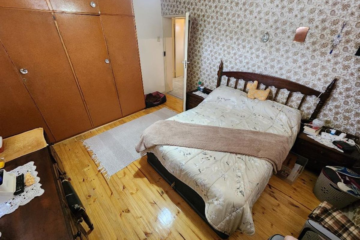 A bedroom featuring built-in wooden wardrobes, patterned wallpaper, and polished timber flooring.