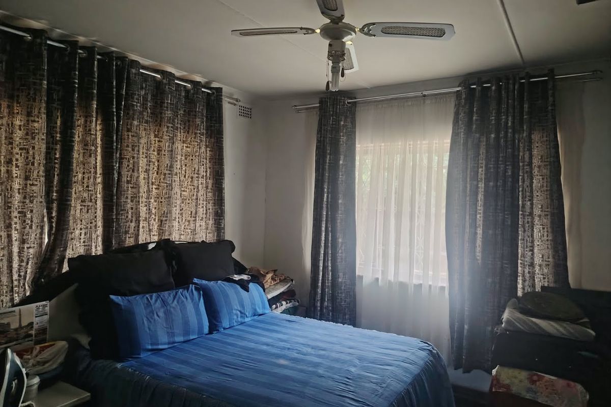 A bedroom featuring a ceiling fan and dual-layered curtain rails, providing a functional space with natural light.