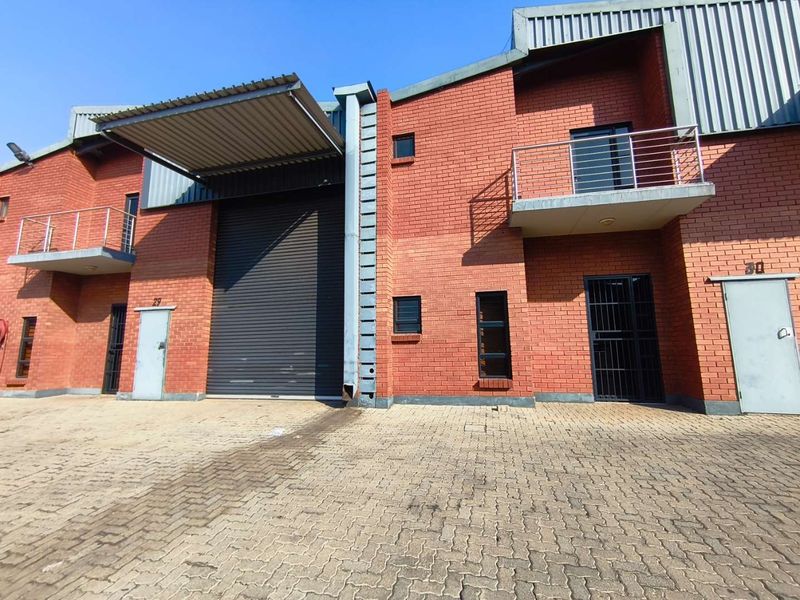 Front view of an industrial unit featuring a large roller shutter door, brick facade, and upper-level balconies with metal railings.