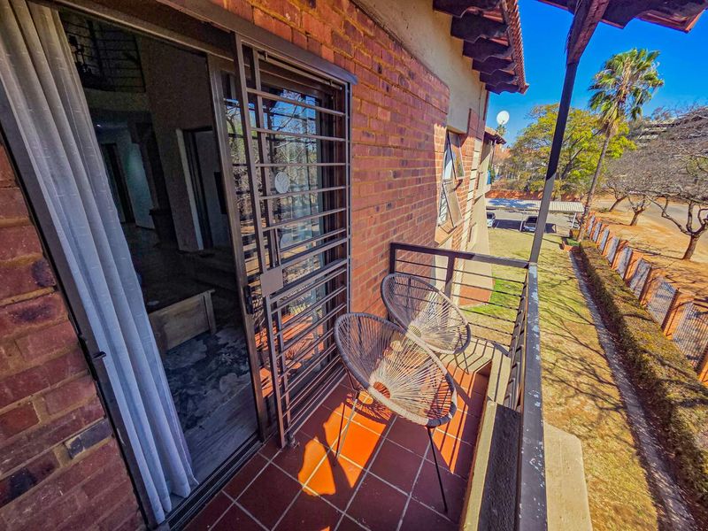 A balcony featuring tiled flooring, a brick exterior wall, and a metal security gate, overlooking the surrounding grounds.