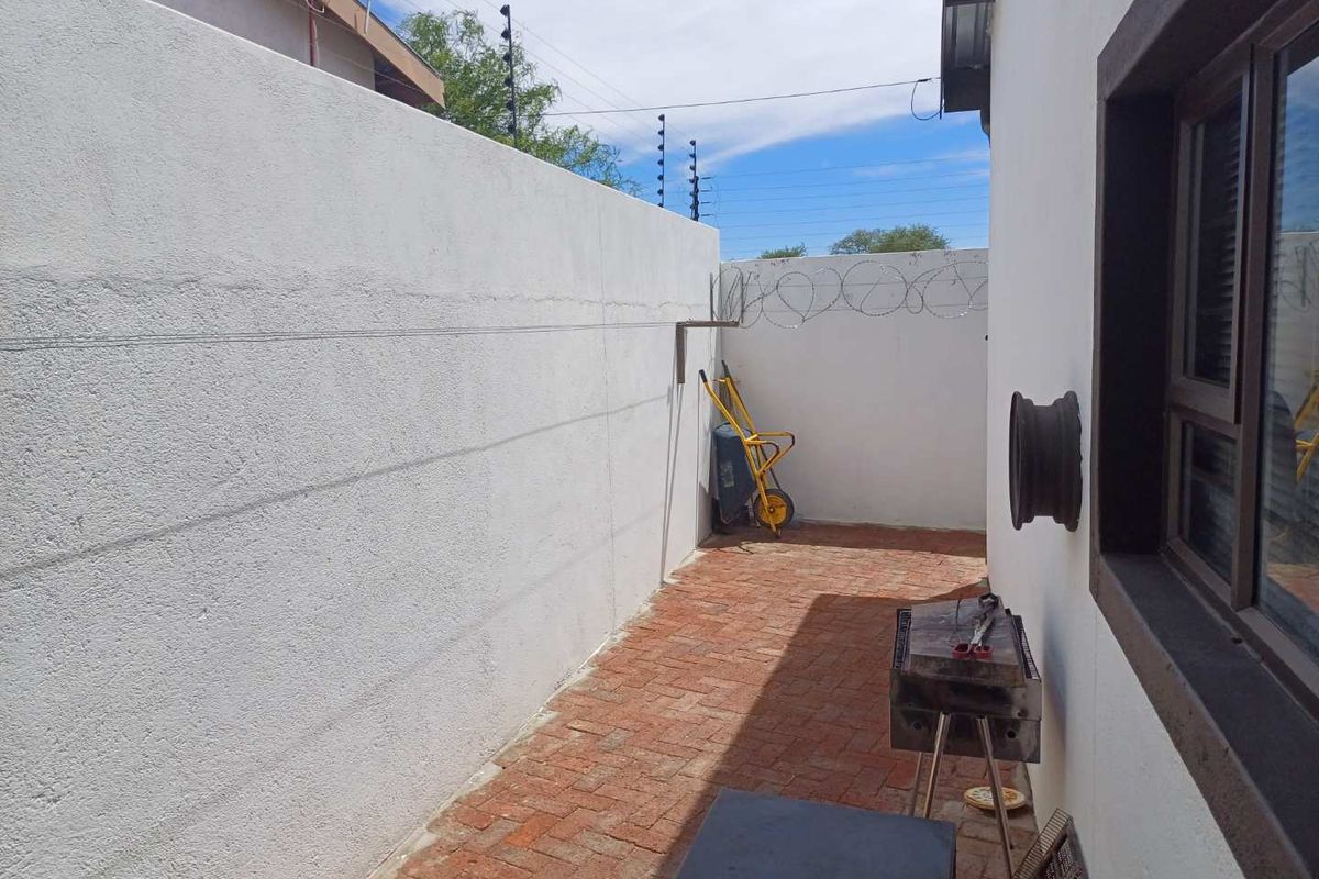 A narrow rear courtyard area featuring brick paving, enclosed by high perimeter walls with security razor wire and electric fencing.