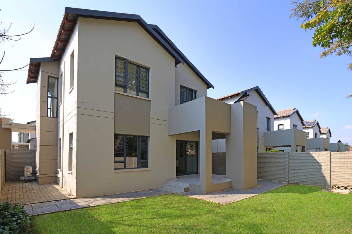 Rear view of a modern townhouse featuring a covered patio, paved walkway, and a well-maintained private garden area.