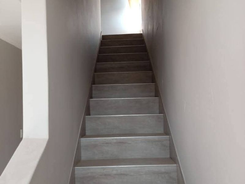 A clean, modern staircase featuring neutral-toned tiled treads and a simple, minimalist design leading to the upper level of the townhouse.