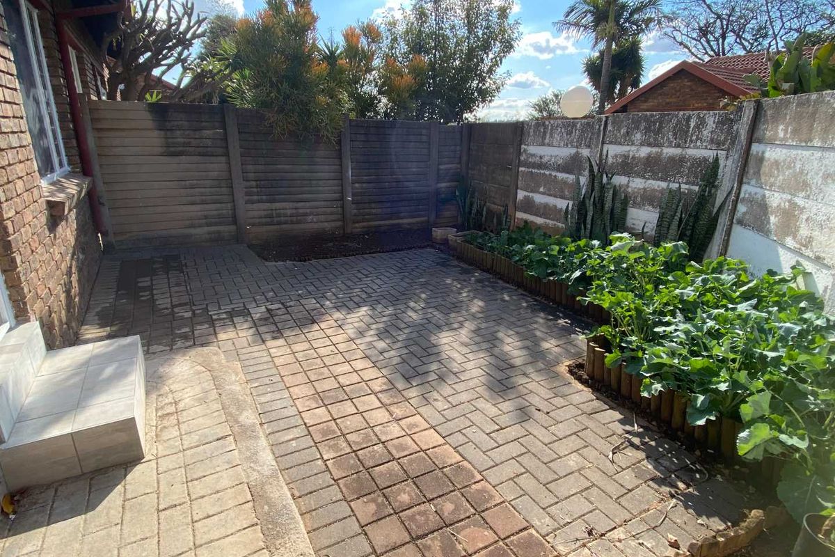 A private rear courtyard featuring paved flooring, a raised garden bed, and a combination of precast concrete and timber boundary fencing.