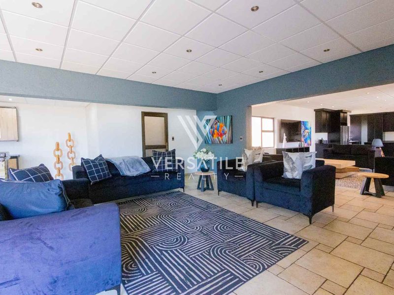 Spacious open-plan living area featuring tiled flooring, recessed lighting, and a connected kitchen space with dark cabinetry.