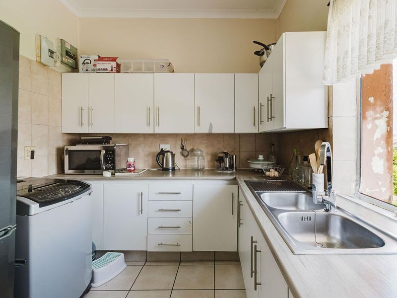 A functional kitchen featuring white cabinetry, laminate countertops, a double stainless steel sink, and tiled backsplash with ceramic floor tiles.