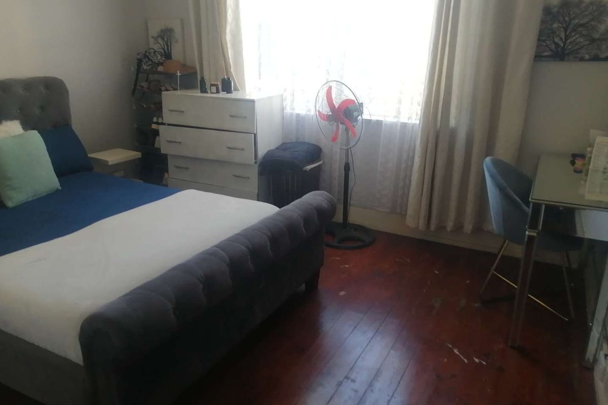 A bedroom featuring original timber flooring and natural light through a large window.