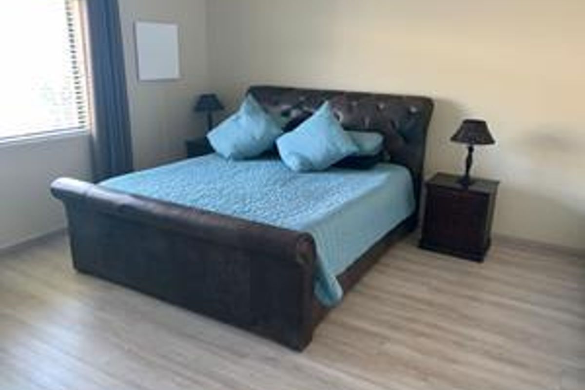 A well-maintained bedroom featuring light-toned laminate flooring and window blinds, providing a neutral and functional living space.