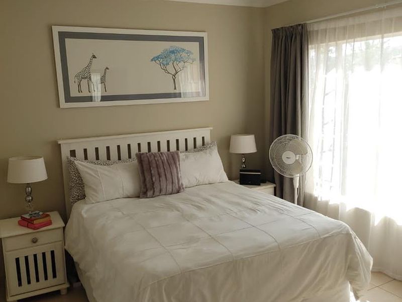 A well-lit bedroom featuring neutral wall tones, tiled flooring, and a large window with curtain tracks, providing a comfortable and functional living space.