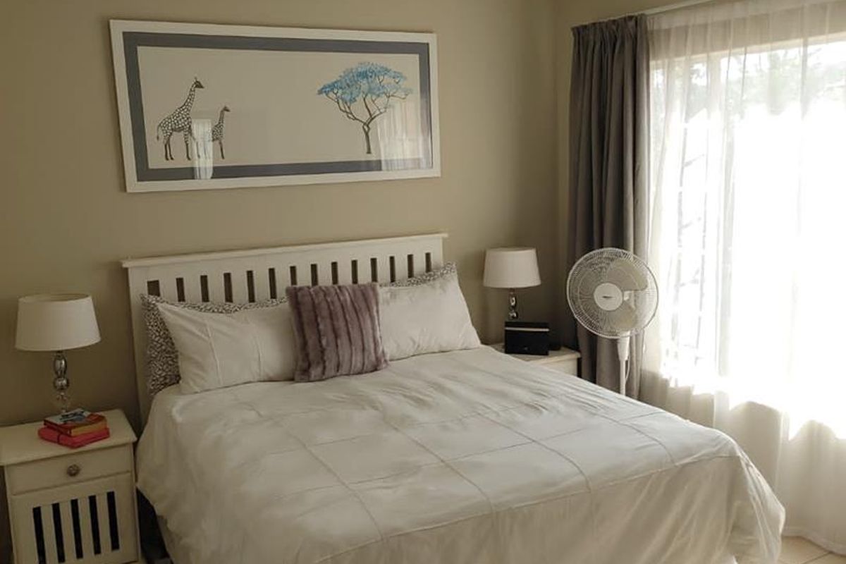 A well-lit bedroom featuring neutral wall tones, tiled flooring, and a large window with curtain tracks, providing a comfortable and functional living space.