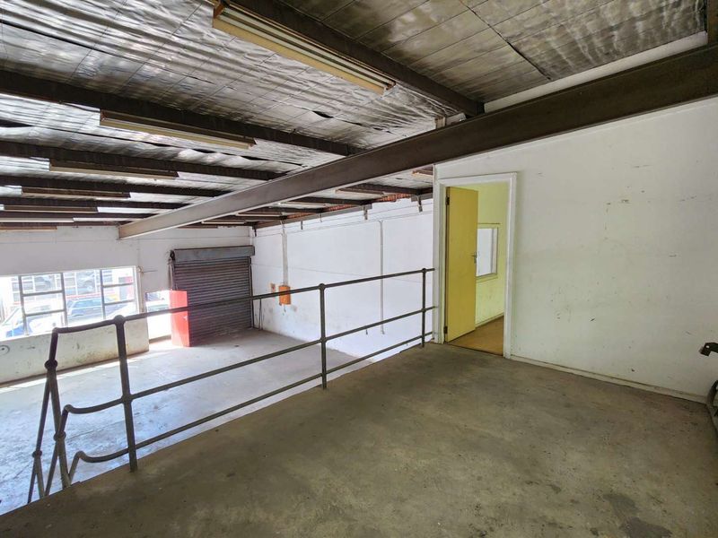 Industrial mezzanine level featuring exposed steel beams, concrete flooring, and a roller shutter door, suitable for storage or workshop use.