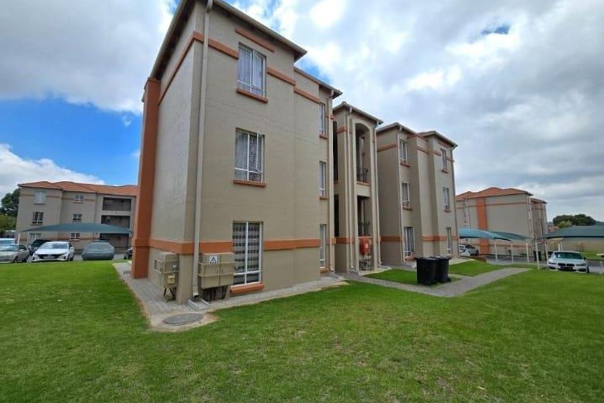 Exterior view of a multi-story townhouse complex featuring painted masonry walls, tiled roofing, and landscaped communal lawn areas.