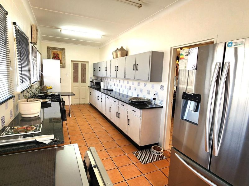 A functional kitchen featuring granite countertops, extensive built-in cabinetry, and a decorative tile backsplash with terracotta-style floor tiles.