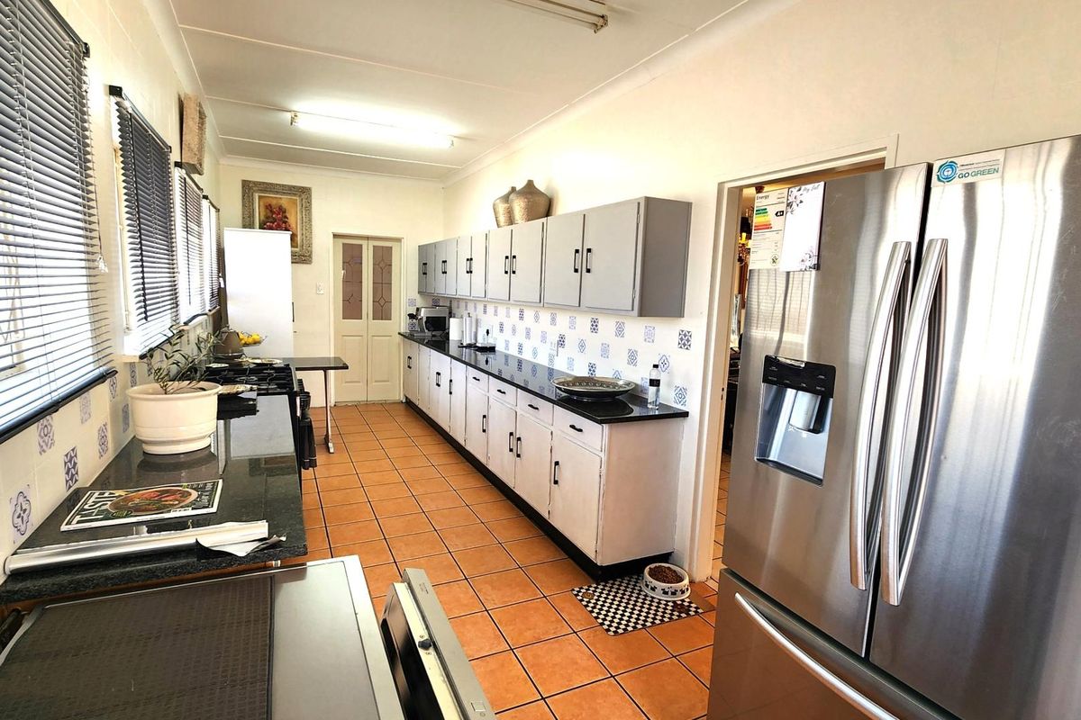 A functional kitchen featuring granite countertops, extensive built-in cabinetry, and a decorative tile backsplash with terracotta-style floor tiles.
