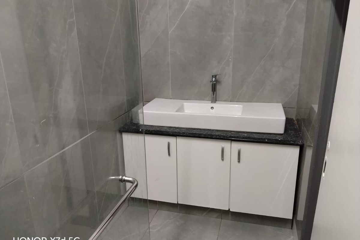 Modern bathroom featuring a sleek vanity cabinet with a stone countertop, basin, and contemporary mixer tap, complemented by large-format grey porcelain wall and floor tiles.