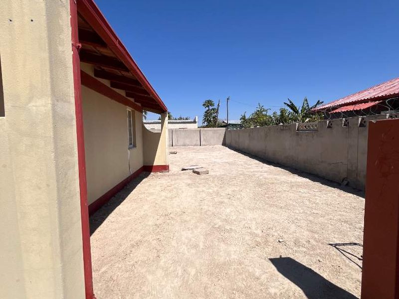 A view of the rear exterior area featuring a concrete boundary wall and unpaved ground, offering potential for landscaping or outdoor development.