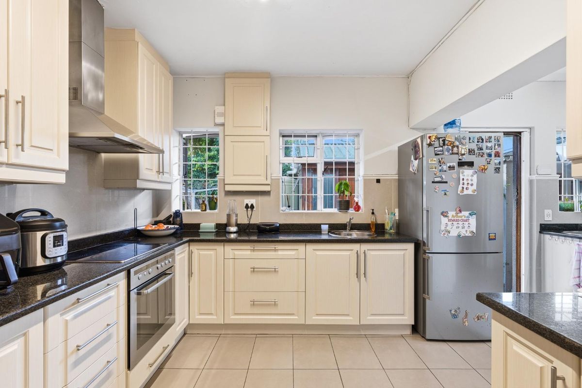 A functional kitchen featuring cream cabinetry, dark granite countertops, a built-in oven, stainless steel extractor fan, and tiled flooring.