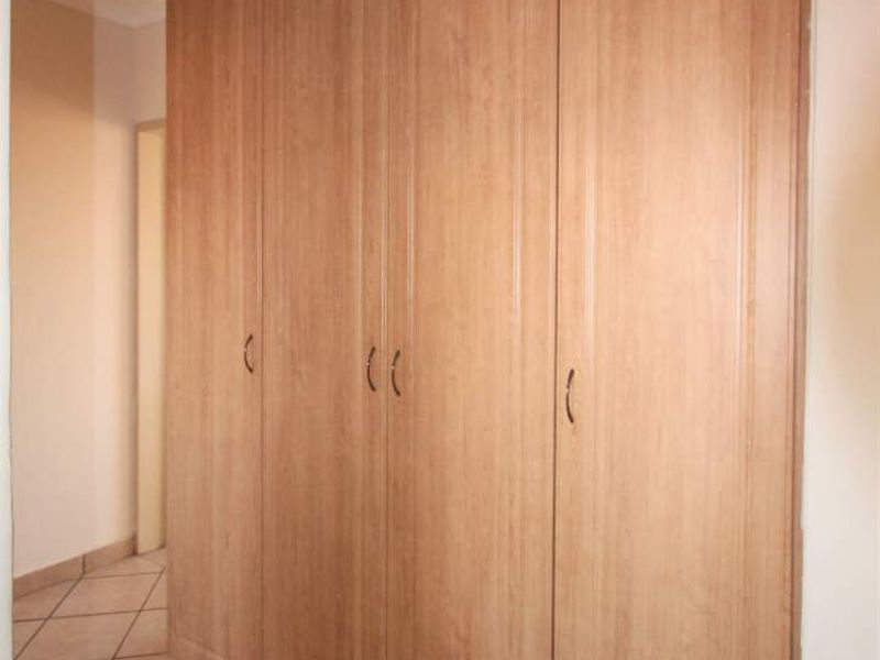 A hallway featuring built-in wooden cupboards and tiled flooring, providing ample storage space within the apartment.