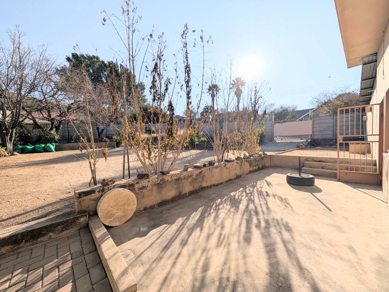 Rear exterior view featuring a concrete patio area, low retaining wall, and a spacious backyard with boundary walling and gated access.