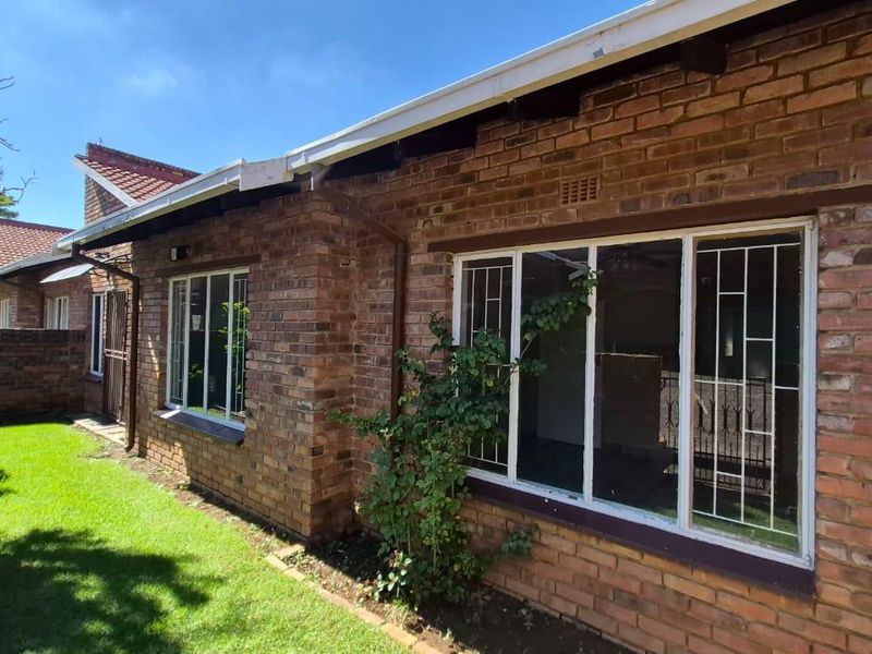 A view of the townhouse rear exterior featuring face-brick walls, white-framed windows with security bars, and a small adjacent garden area.