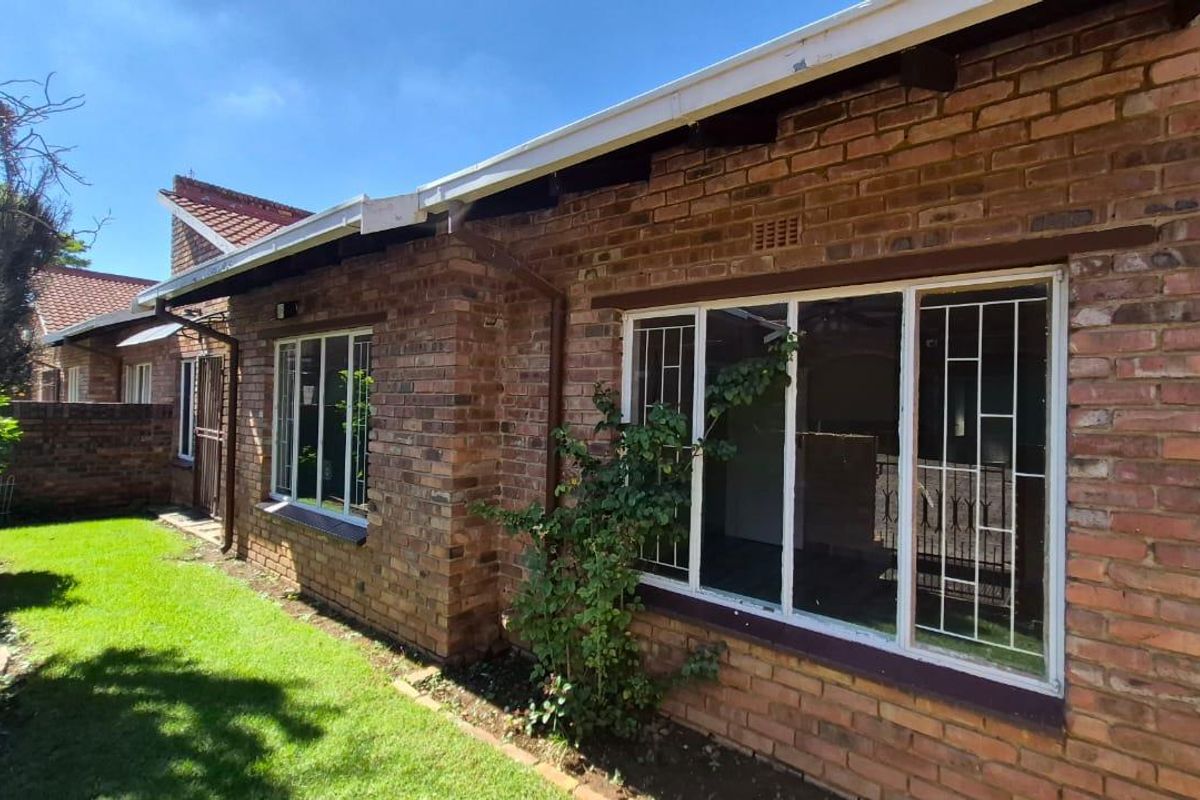 A view of the townhouse rear exterior featuring face-brick walls, white-framed windows with security bars, and a small adjacent garden area.