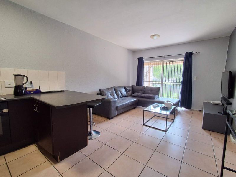 Open-plan living area featuring tiled flooring, a compact kitchen with dark cabinetry, and a sliding glass door leading to an outdoor space.