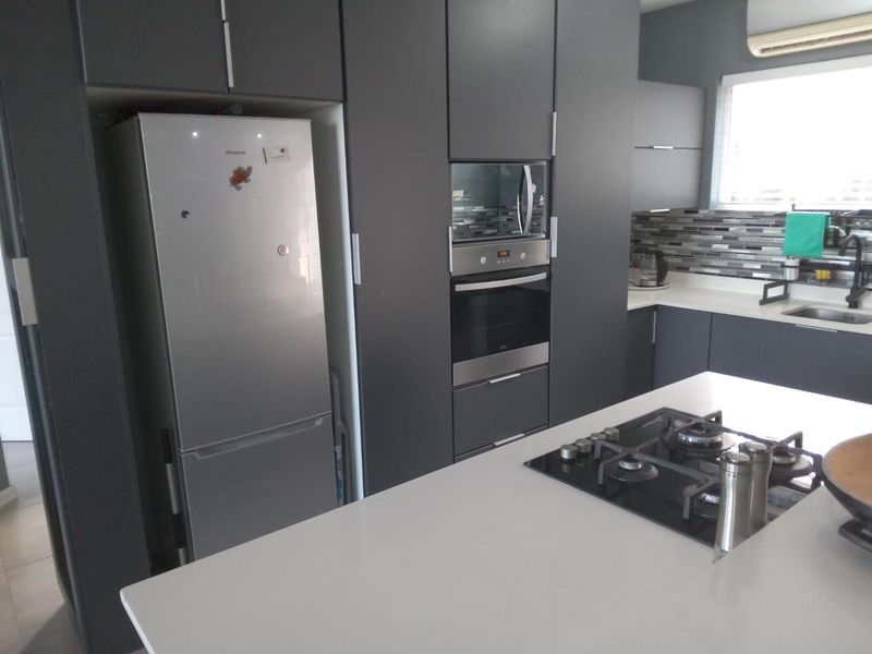 Modern kitchen featuring dark cabinetry, stone countertops, a central island with a gas cooktop, built-in oven, microwave, and a stylish mosaic tile backsplash.