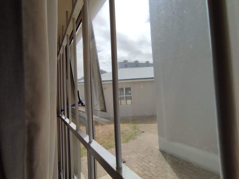 View from an interior window looking out onto a paved courtyard and neighbouring building, featuring security bars on the window frame.