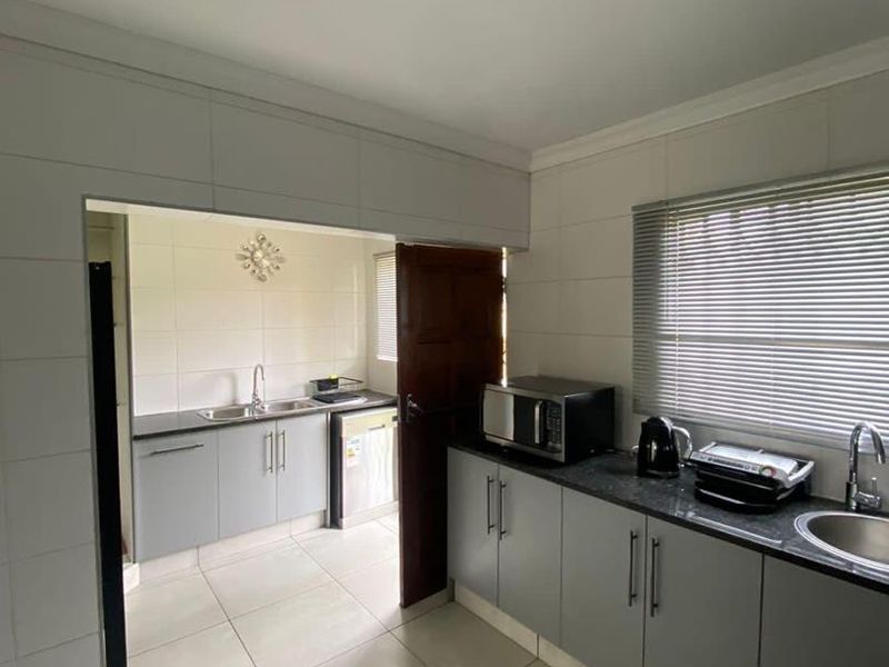 A functional kitchen featuring grey cabinetry, granite countertops, tiled finishes, and a secondary scullery area, providing ample workspace and storage.