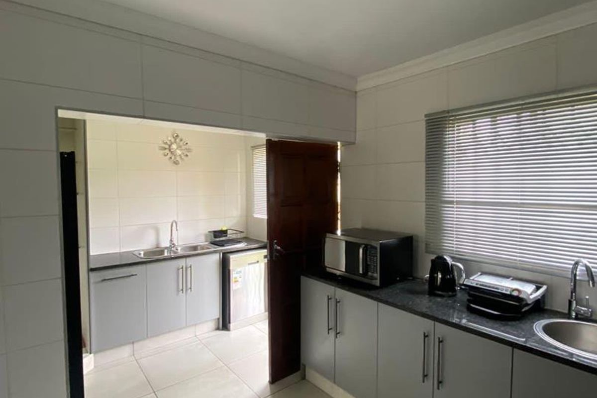 A functional kitchen featuring grey cabinetry, granite countertops, tiled finishes, and a secondary scullery area, providing ample workspace and storage.