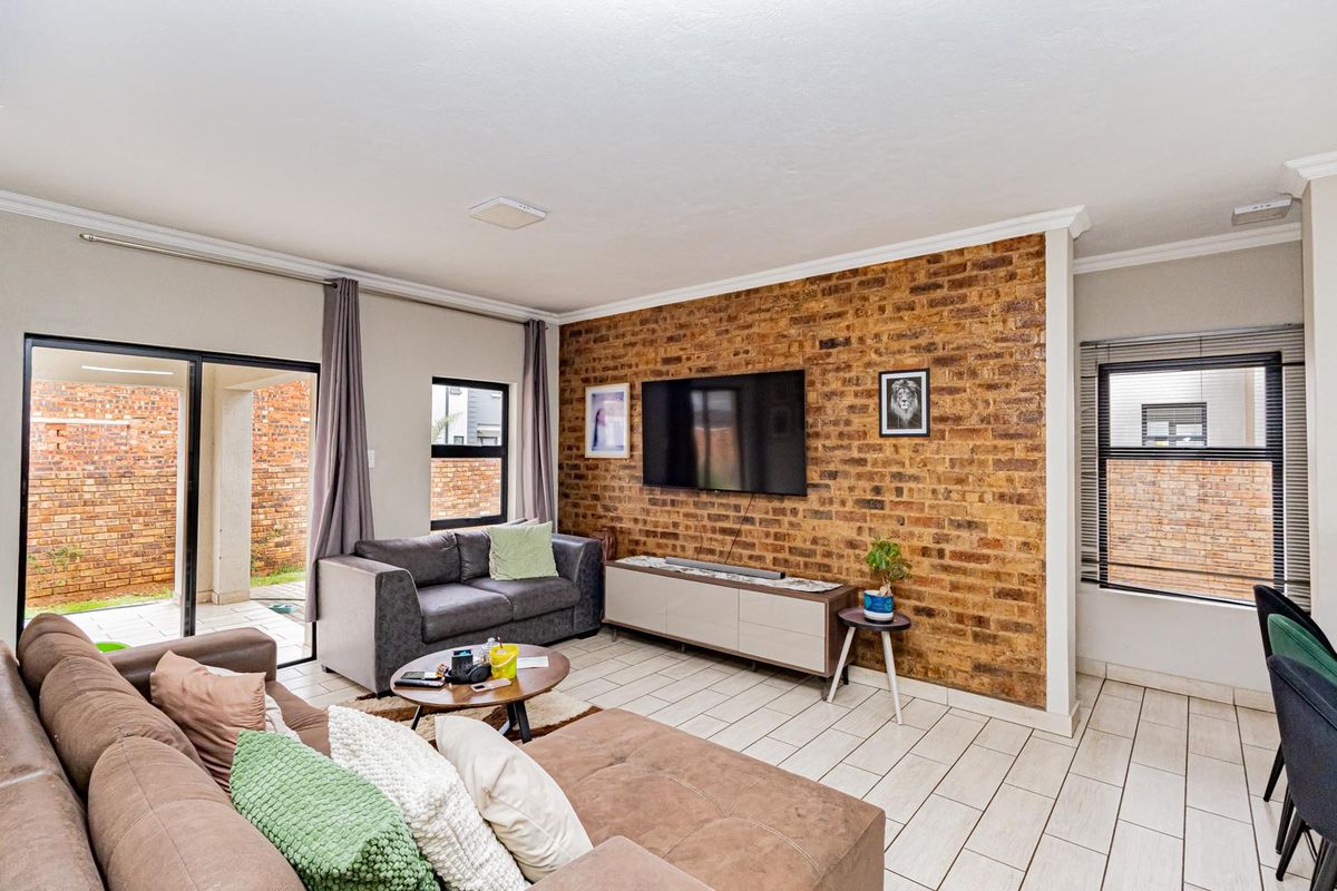 A bright living room featuring a prominent exposed brick feature wall, tiled flooring, and large sliding glass doors providing access to the outdoor area.