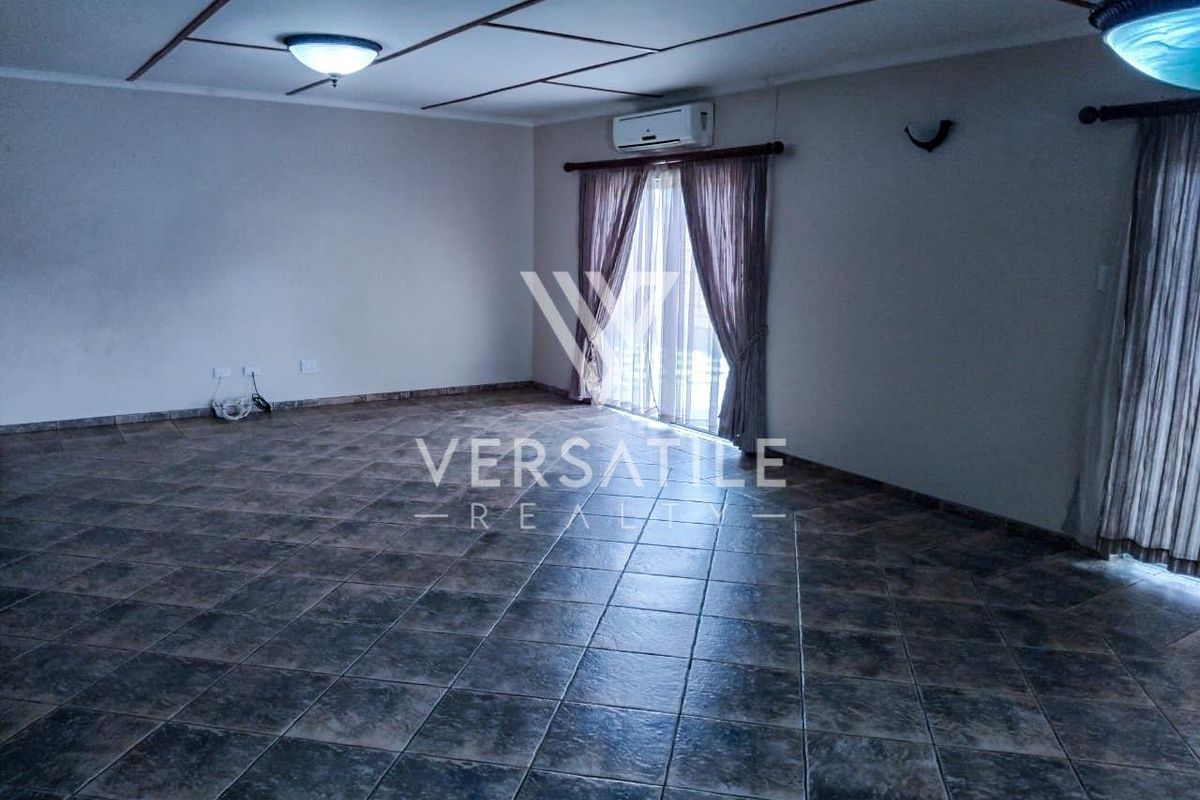 Spacious living area featuring tiled flooring, a wall-mounted air conditioning unit, and sliding glass doors providing access to the exterior.