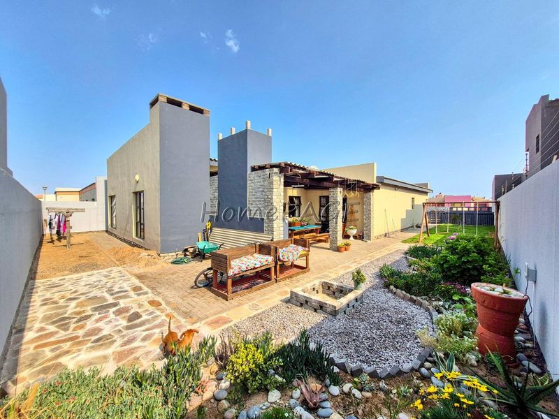 Rear view of the property featuring a paved patio area with a timber pergola, stone fire pit, and a well-maintained landscaped garden.