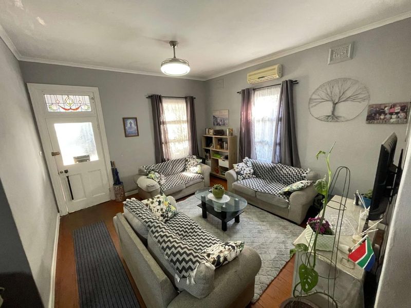 A comfortable living room featuring timber flooring, a split-system air conditioner, and a classic front door with leaded glass detailing.